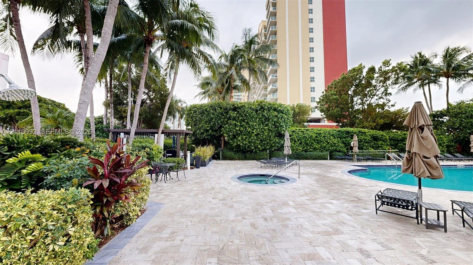 Outdoor pool and hot tub area featuring stone-paver decking and mature landscaping