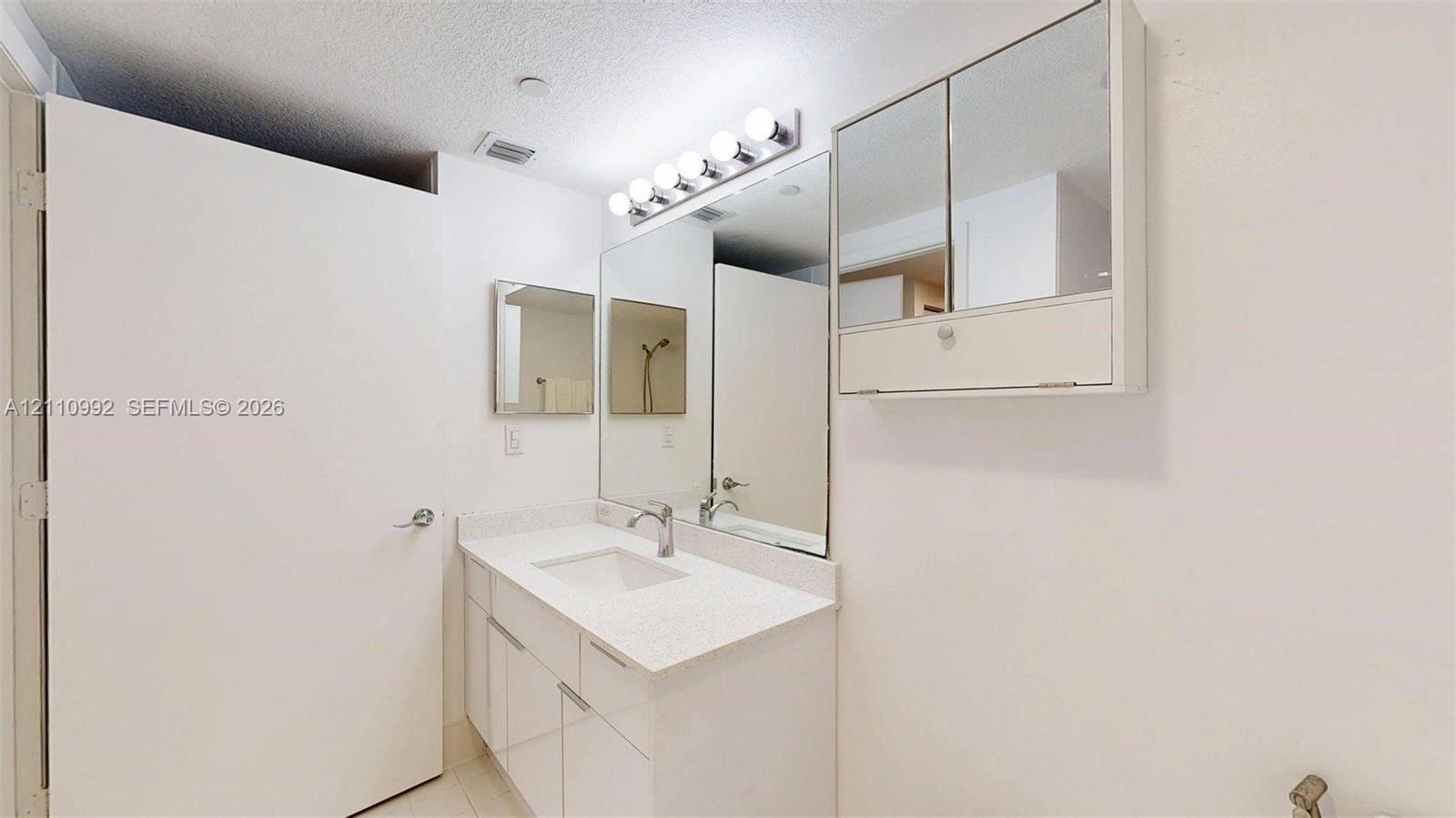 Bathroom vanity featuring a solid surface countertop, integrated rectangular sink, chrome fixtures, built-in medicine cabinet, and wall-mounted multi-bulb lighting