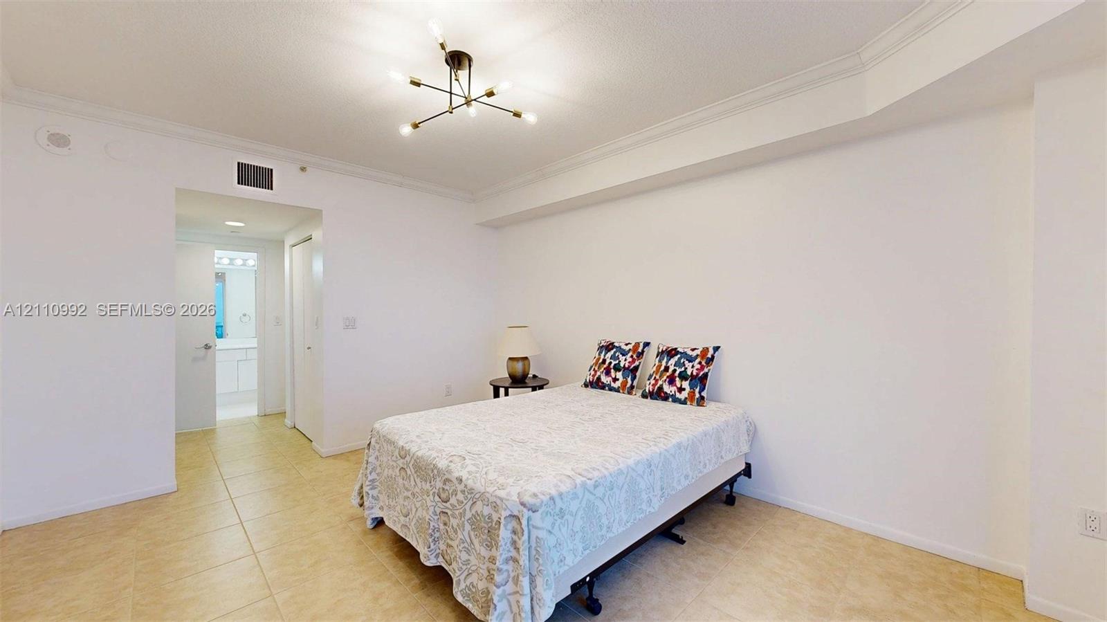 Neutral-toned tile flooring, tray ceiling with crown molding, and modern multi-arm sputnik-style overhead lighting