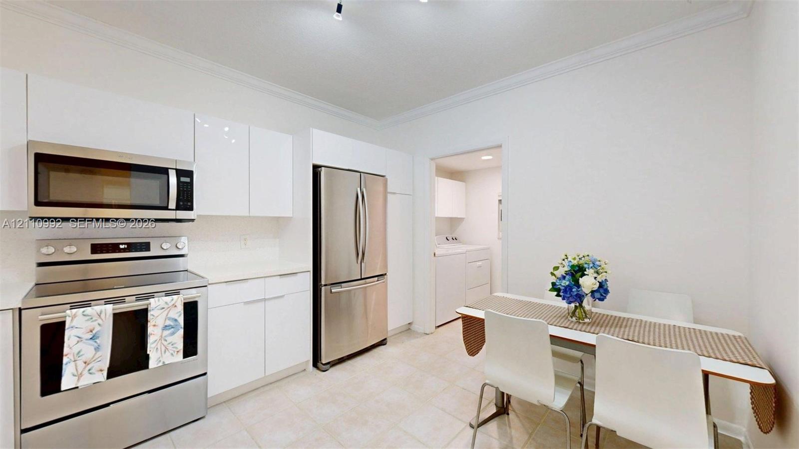 Kitchen featuring white flat-panel cabinetry, stainless steel appliances, solid surface countertops, and tile flooring