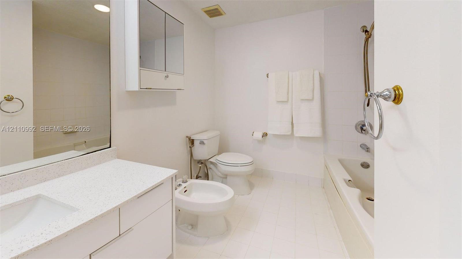 Bathroom featuring a vanity with a white countertop and integrated sink, a built-in medicine cabinet, a bidet, and a bathtub with a handheld shower fixture