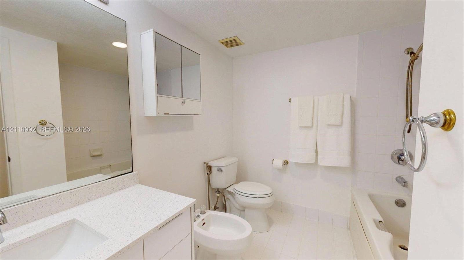 Bathroom featuring a stone-surface vanity countertop, an integrated rectangular sink, a mirrored medicine cabinet, a bidet, and a tile-surround shower and tub combination