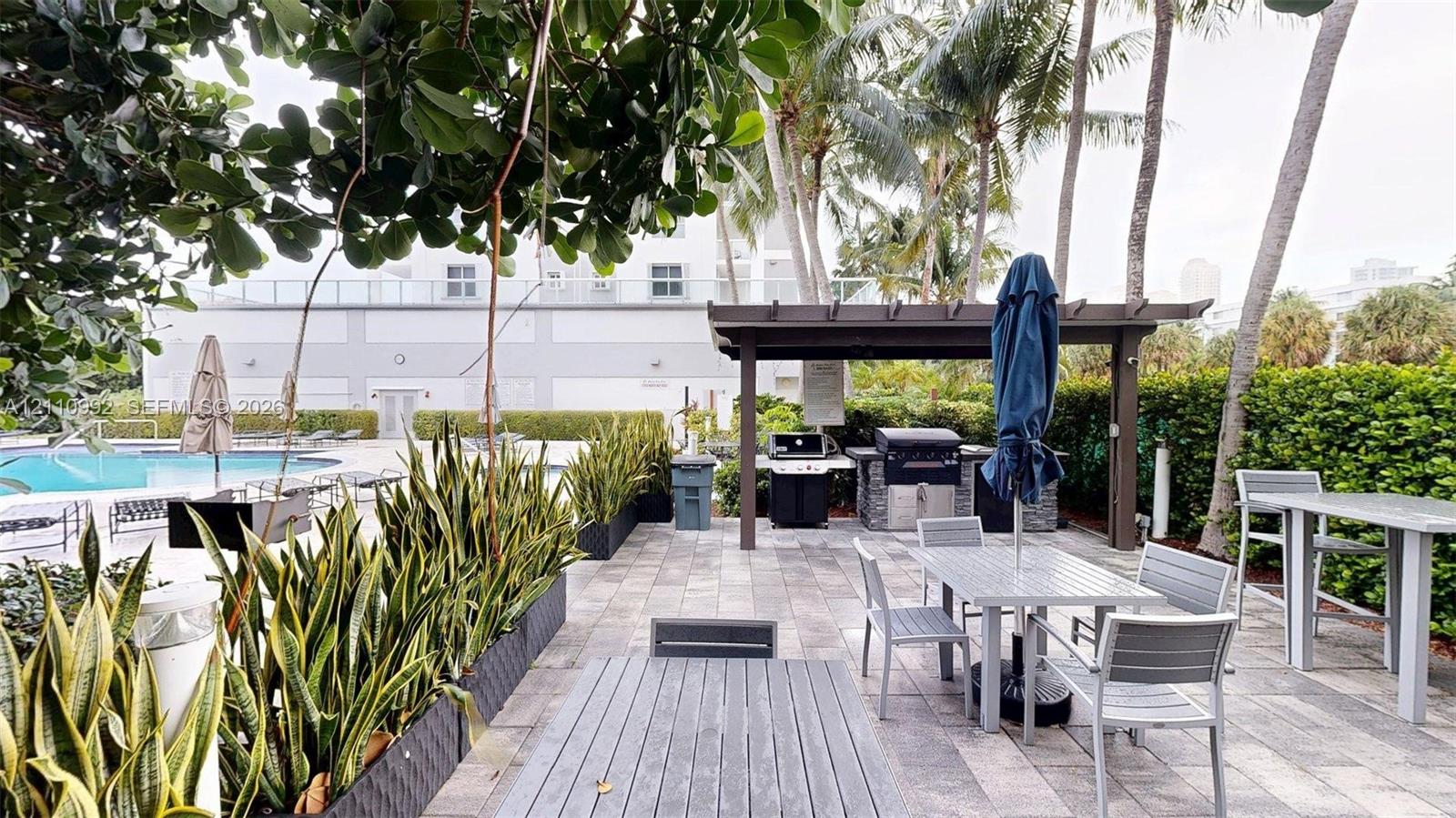 Outdoor patio area featuring a paved stone floor, a covered pergola with a built-in barbecue station, and integrated planters