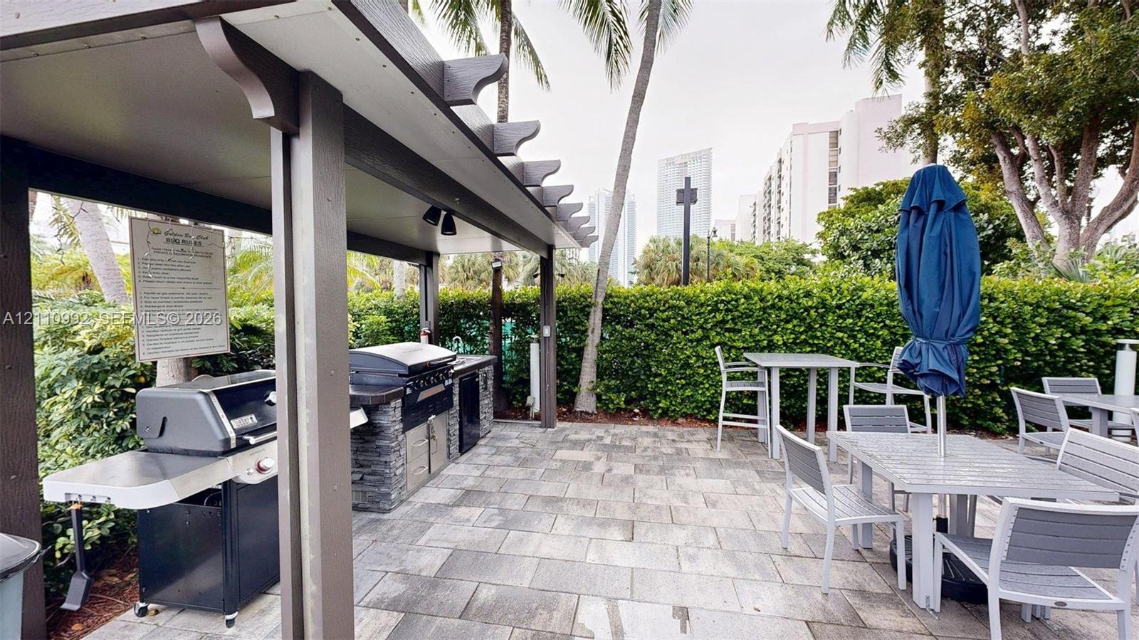 Covered outdoor kitchen featuring built-in stainless steel grills, stone-finish base cabinetry, and paved patio flooring
