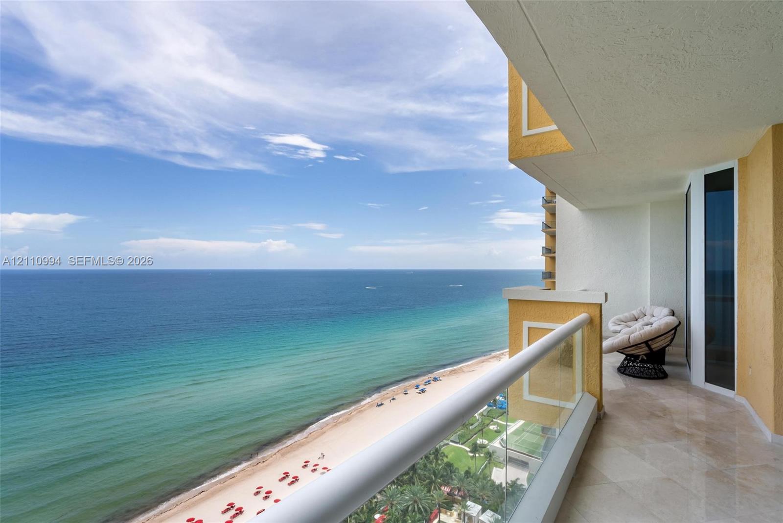 Covered balcony featuring natural stone flooring, glass railing, and textured exterior wall finish, overlooking the coastline