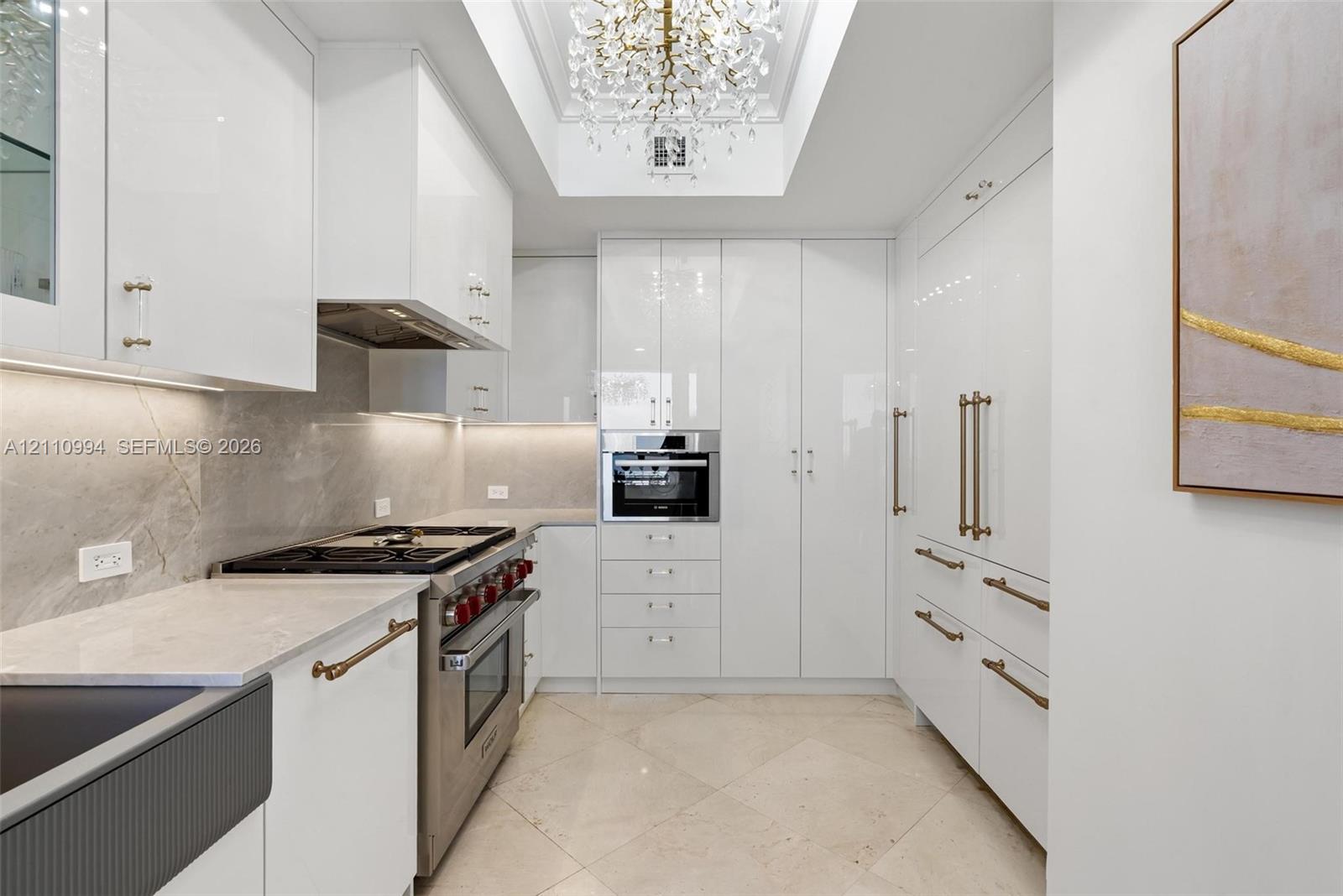 Gourmet kitchen featuring high-gloss cabinetry, stone-finish countertops, tile flooring, stainless steel professional-grade range, and a coffered ceiling with crystal chandelier