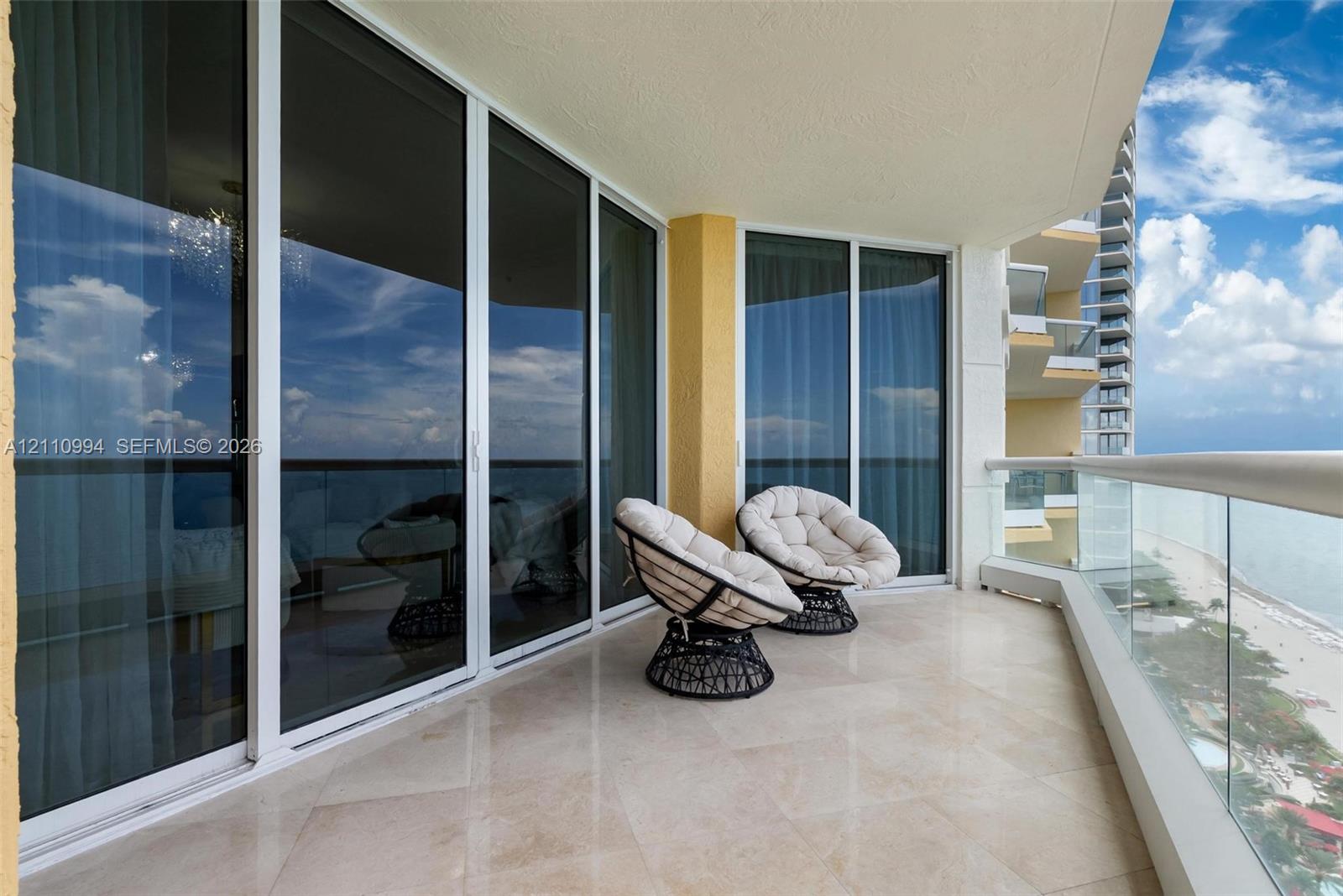Covered balcony featuring stone tile flooring, floor-to-ceiling glass sliding doors, and a transparent glass pane railing