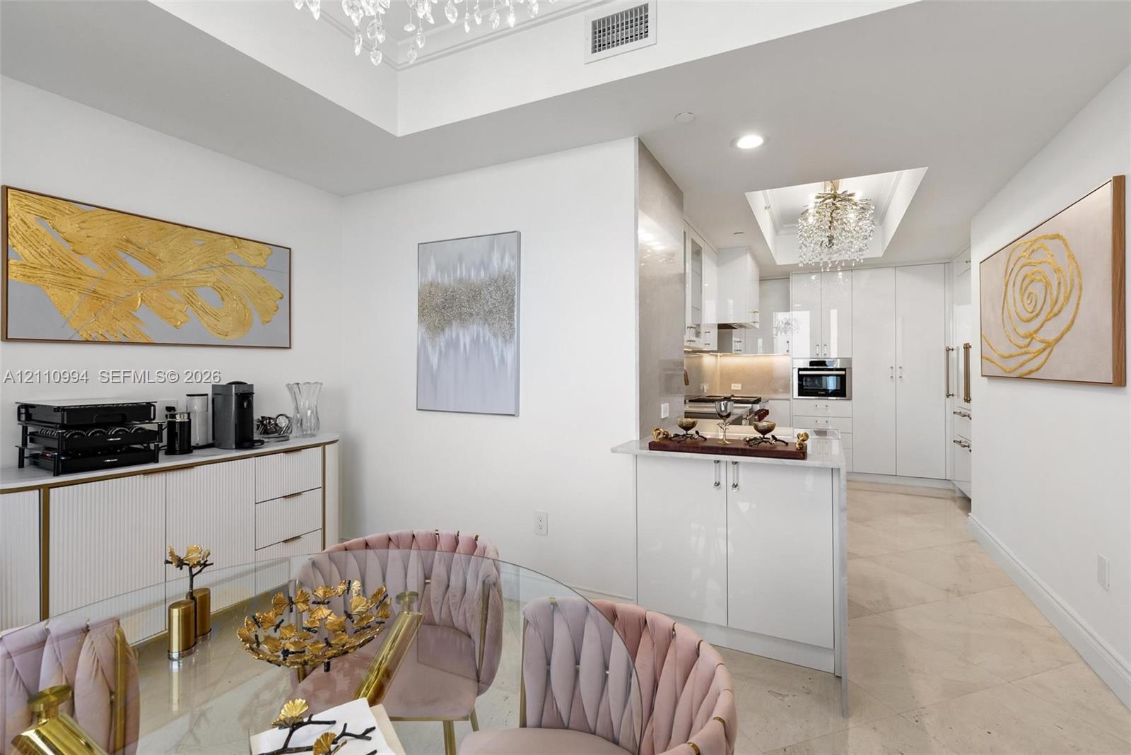 Kitchen featuring high-gloss cabinetry, stone tile flooring, tray ceilings with crystal chandeliers, and a built-in buffet