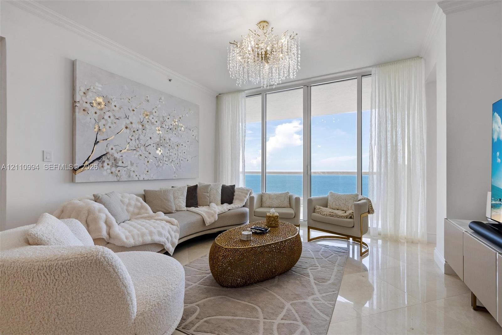 Floor-to-ceiling windows featuring ocean panoramas, polished tile flooring, and a tiered crystal chandelier