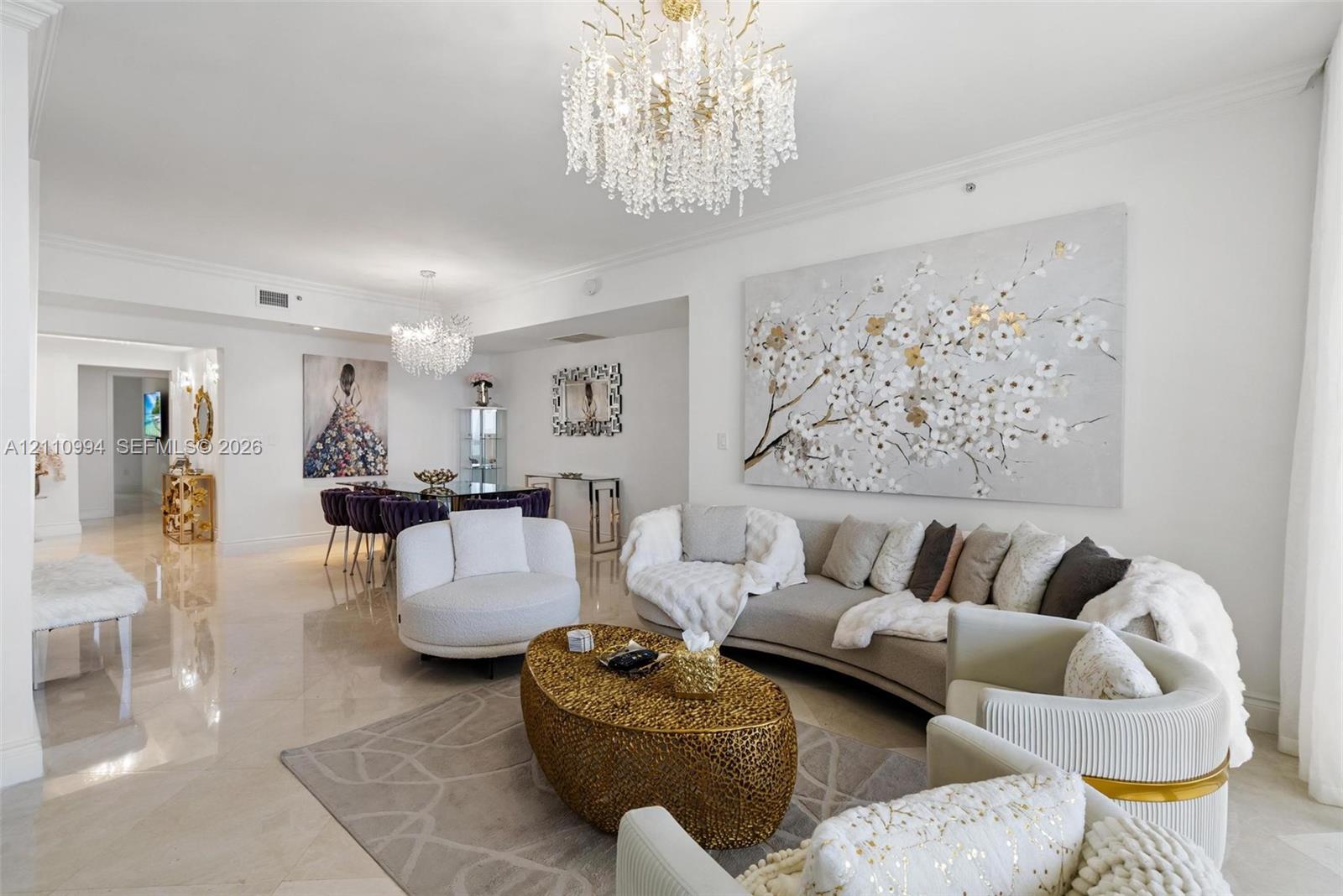 Open-concept interior featuring large-format polished stone flooring, crown molding, and dual ornate crystal chandeliers Open-concept interior featuring large-format polished stone flooring, crown molding, and dual ornate crystal chandeliers
