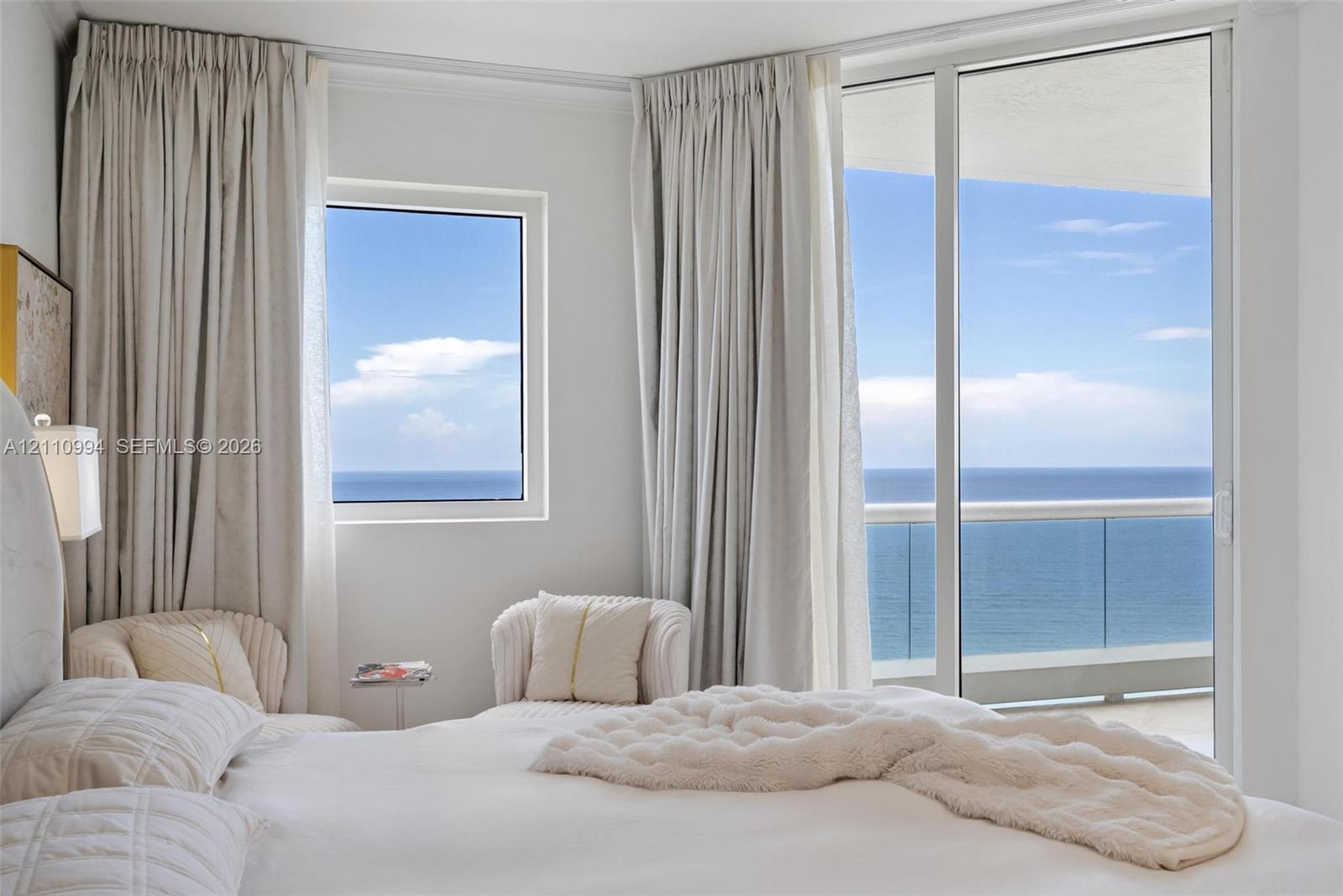 Floor-to-ceiling windows, sliding glass door with glass railing balcony, and ocean horizon backdrop
