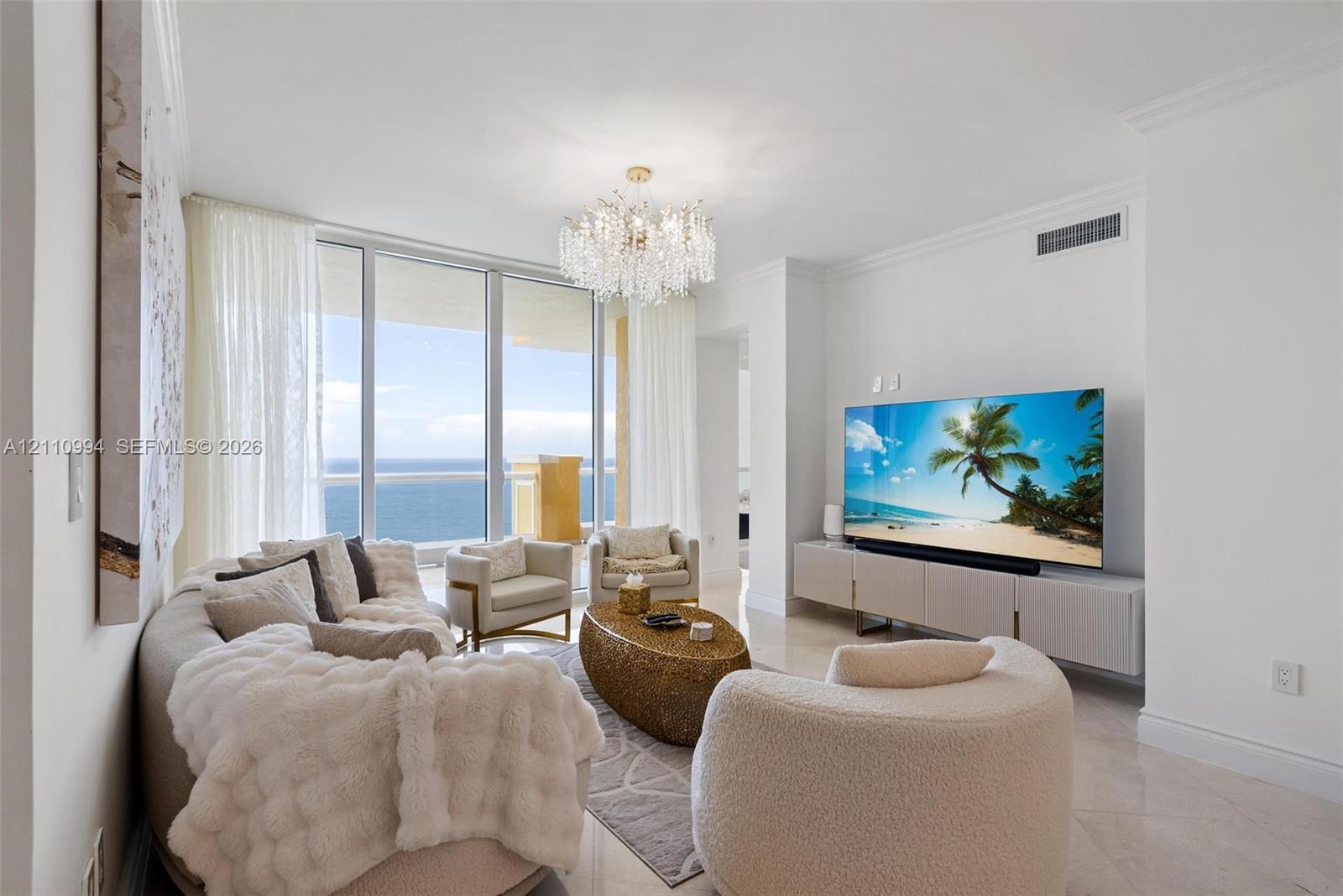 Living space featuring floor-to-ceiling glass panel doors, polished stone flooring, a multi-tiered crystal chandelier, and crown molding Living space featuring floor-to-ceiling glass panel doors, polished stone flooring, a multi-tiered crystal chandelier, and crown molding