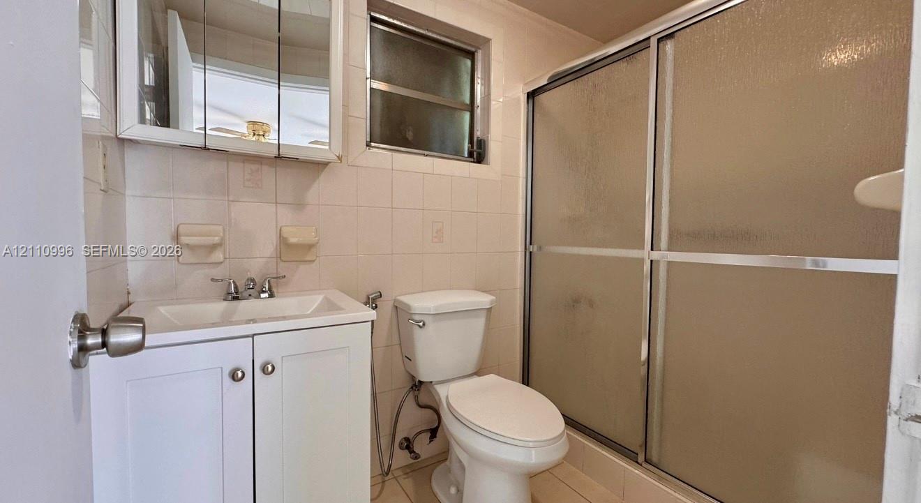 Bathroom featuring a white vanity cabinet, a wall-mounted medicine cabinet with a mirror, a ceramic tile shower enclosure with sliding glass doors, and white wall tile