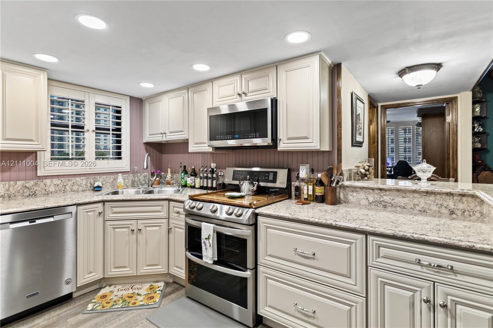 Kitchen featuring light-toned cabinetry, stone-finish countertops, stainless steel appliances, recessed lighting, and built-in shutter-style window coverings