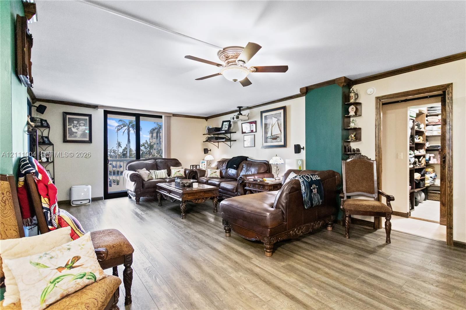 Living area featuring wood-finish flooring, a ceiling fan with integrated lighting, built-in corner shelving, and a sliding glass door