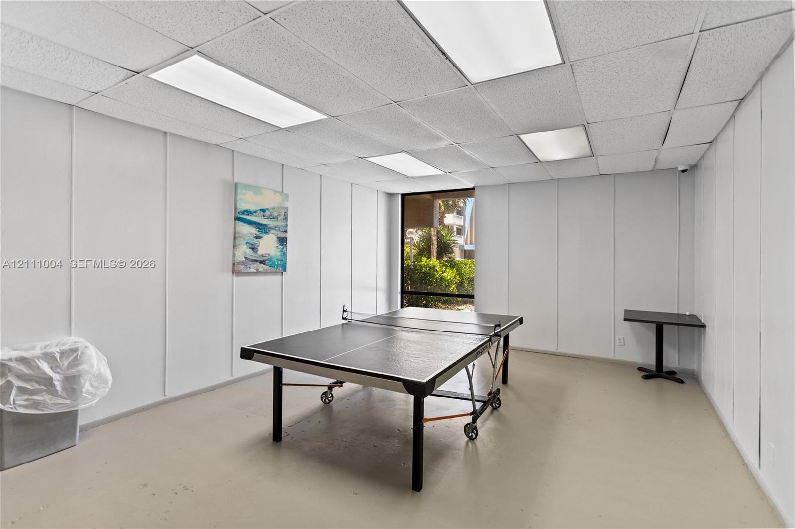 Interior room featuring white paneled walls, a drop ceiling with recessed lighting, smooth flooring, and a window with exterior greenery