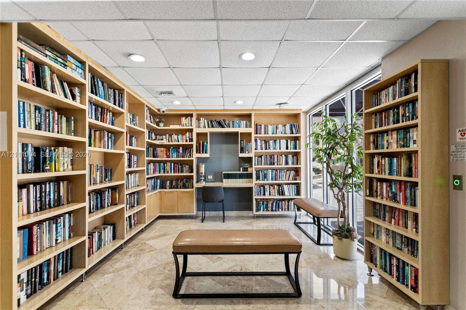 Floor-to-ceiling wood-finish built-in shelving, integrated desk workspace, polished stone flooring, recessed ceiling lighting, and expansive floor-to-ceiling windows