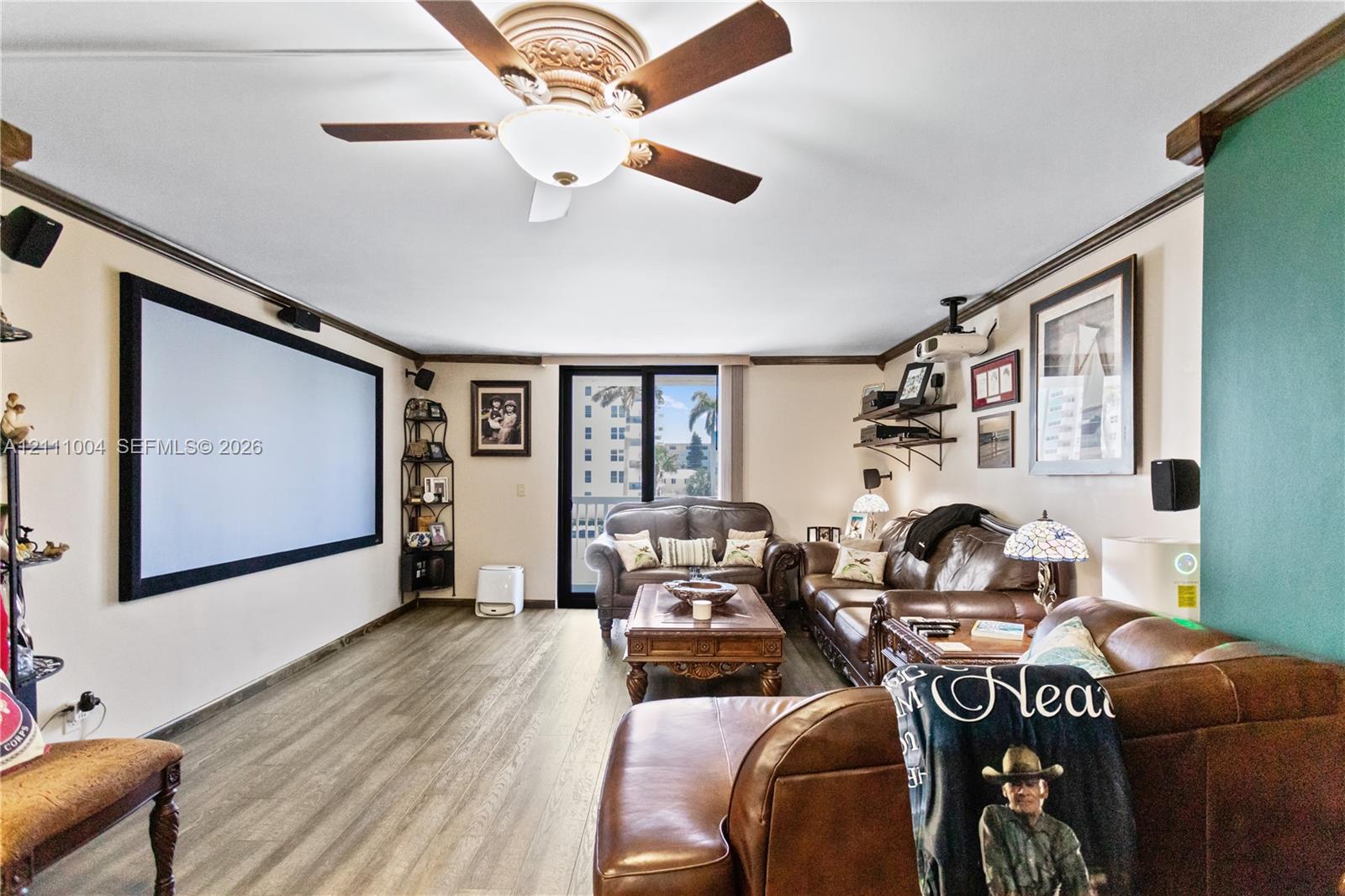 Wood-finish flooring, ceiling fan with integrated lighting, wall-mounted projection screen, and sliding glass door with external access