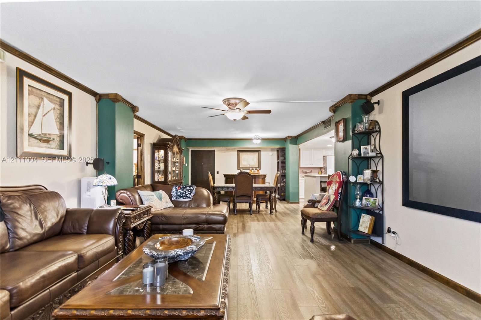 Living area featuring wood-finish flooring, crown molding, dual-toned wall accents, and a central ceiling fan with an integrated light fixture