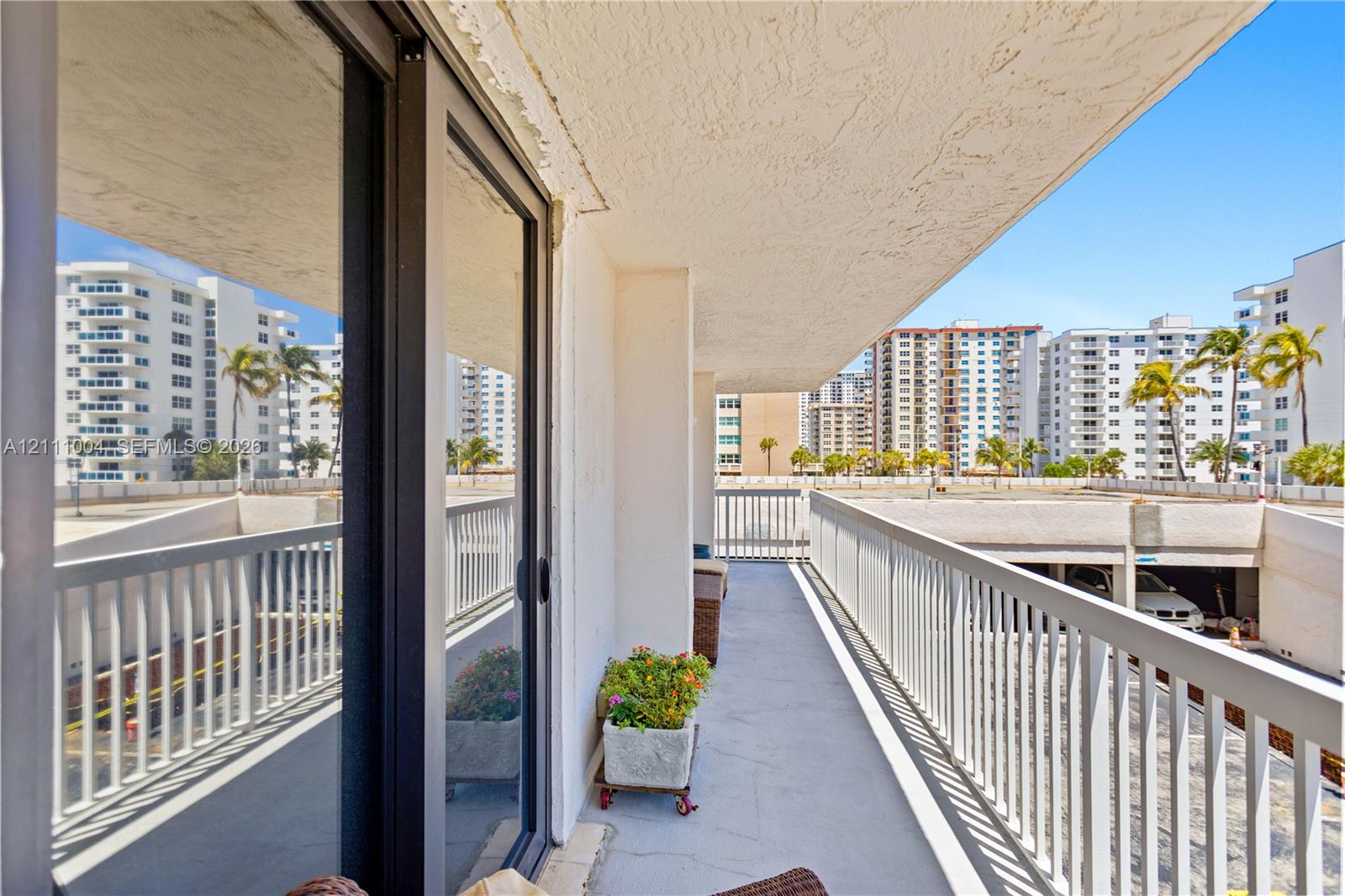 Covered balcony featuring concrete flooring, sliding glass door access, and white metal railings