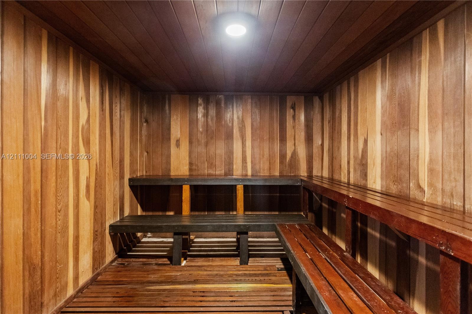 Sauna featuring wood-paneled walls, tongue-and-groove ceiling, multi-level slatted benches, and recessed lighting