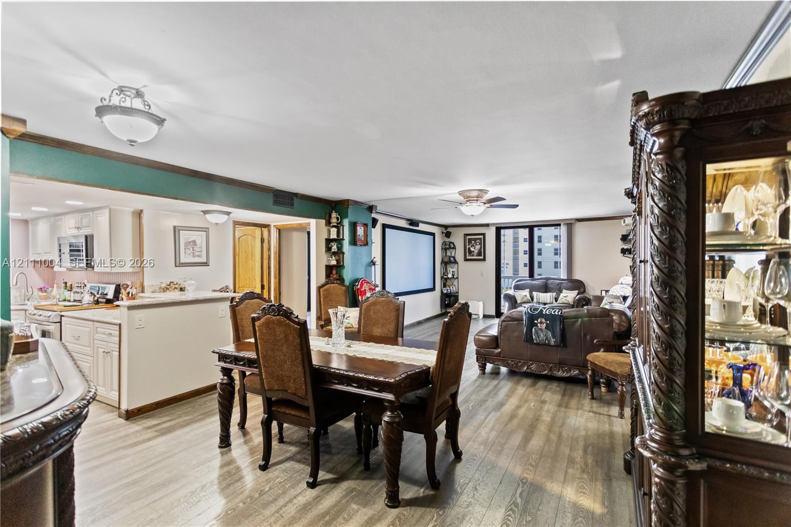 Open-concept interior featuring wood-finish flooring, crown molding, ceiling fans, and a mounted projector screen