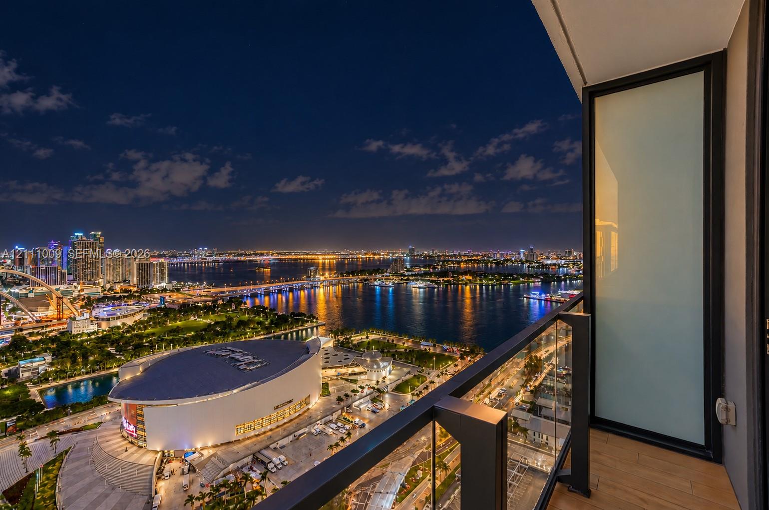 Private balcony featuring glass-panel railings, wood-finish flooring, and expansive urban waterfront scenery