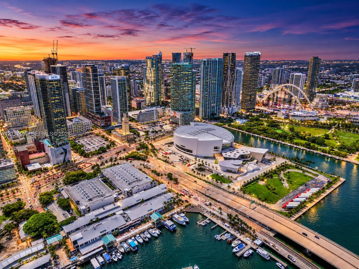 Aerial perspective of metropolitan skyline featuring high-rise architecture, proximity to waterfront, urban park spaces, and paved thoroughfares