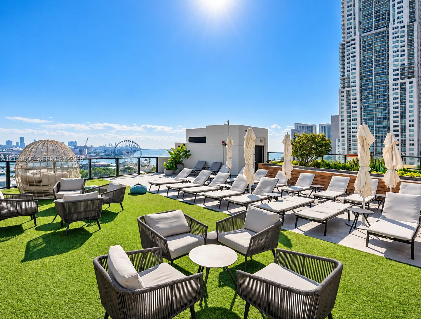 Rooftop terrace featuring synthetic turf, stone tile paving, built-in planters with greenery, and a black metal railing