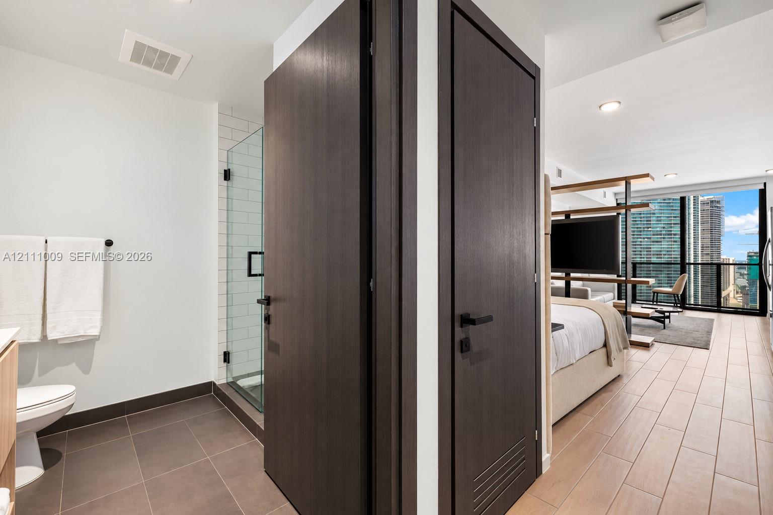 Bathroom featuring a glass-enclosed shower with subway tile surround and dark-toned floor tiling, paired with wood-finish flooring throughout the space and floor-to-ceiling windows