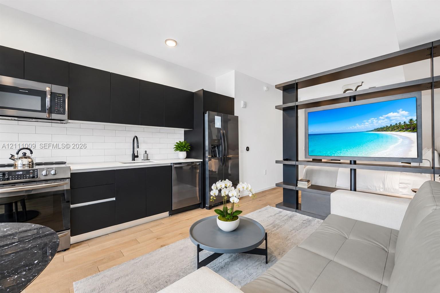 Kitchen featuring matte black flat-panel cabinetry, white subway tile backsplash, stainless steel appliances, light-toned wood-finish flooring, and a built-in floor-to-ceiling metal shelving unit