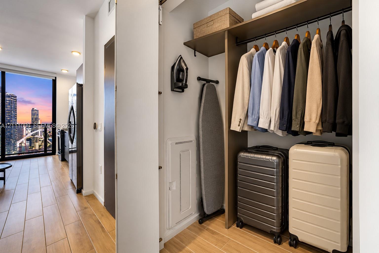 Custom closet system featuring built-in wood-finish shelving and hanging rods, wood-finish flooring, and floor-to-ceiling windows with urban skyline scenery
