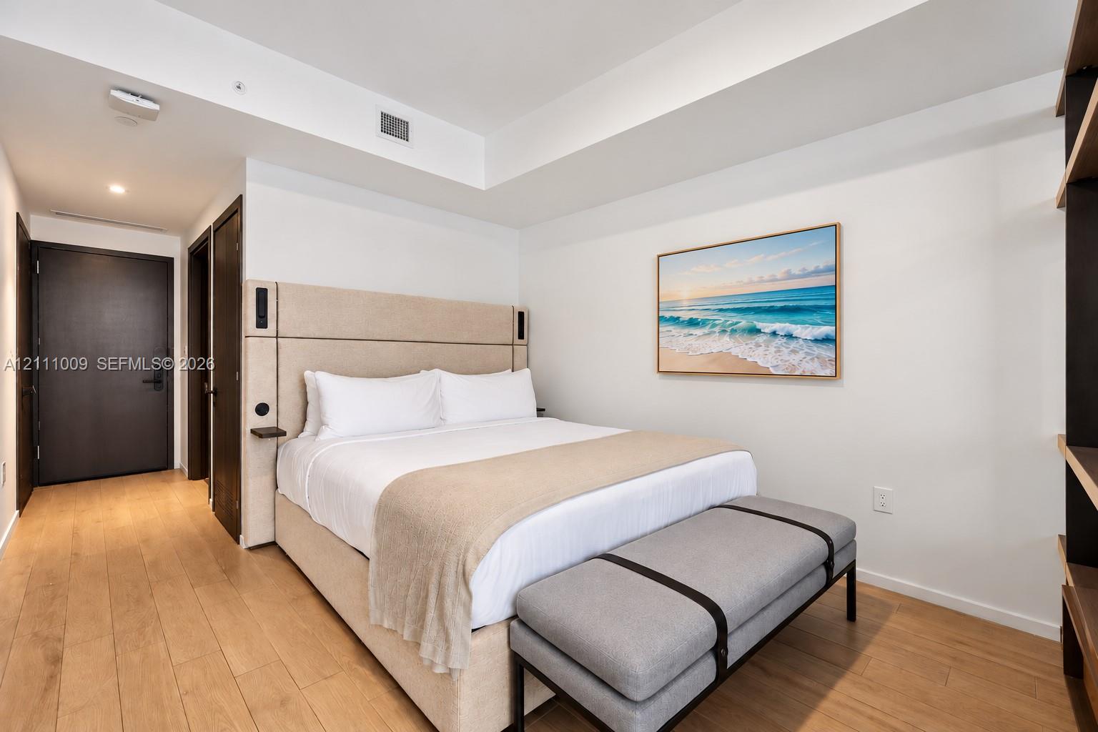 Wood-finish flooring, recessed tray ceiling, built-in headboard with integrated lighting and shelving, and solid-core interior doors