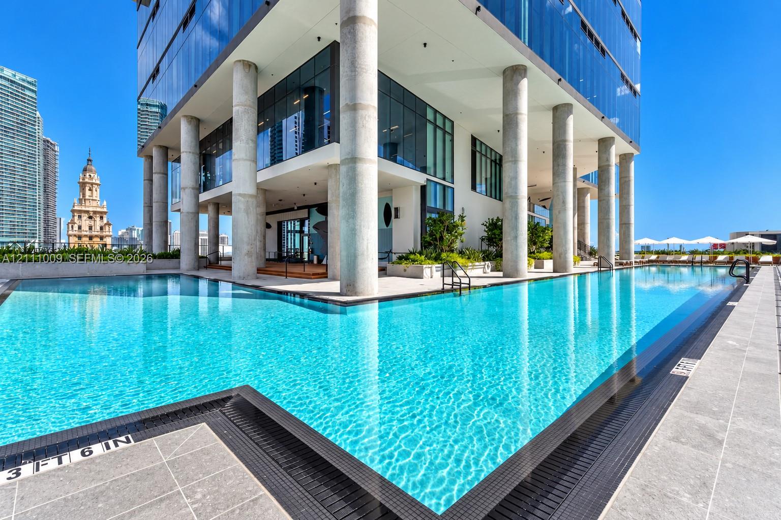 Swimming pool featuring a stone-tiled deck, glass curtain walls, and structural concrete columns