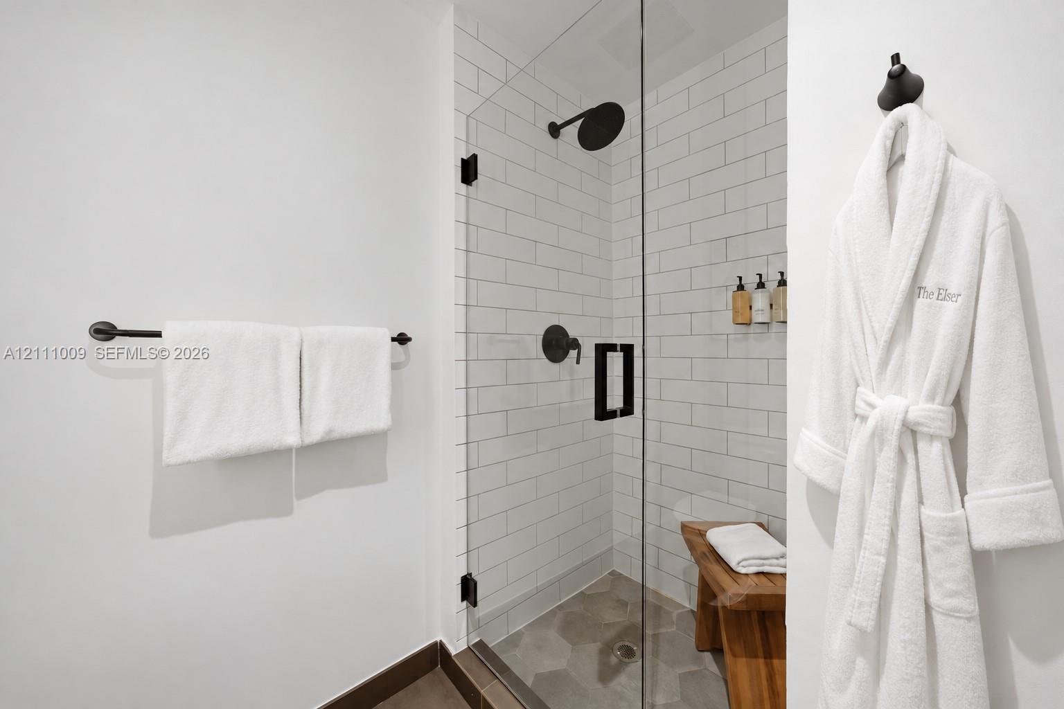 Walk-in shower featuring white subway tile surround, frameless glass door, matte black fixtures, and hexagonal floor tile
