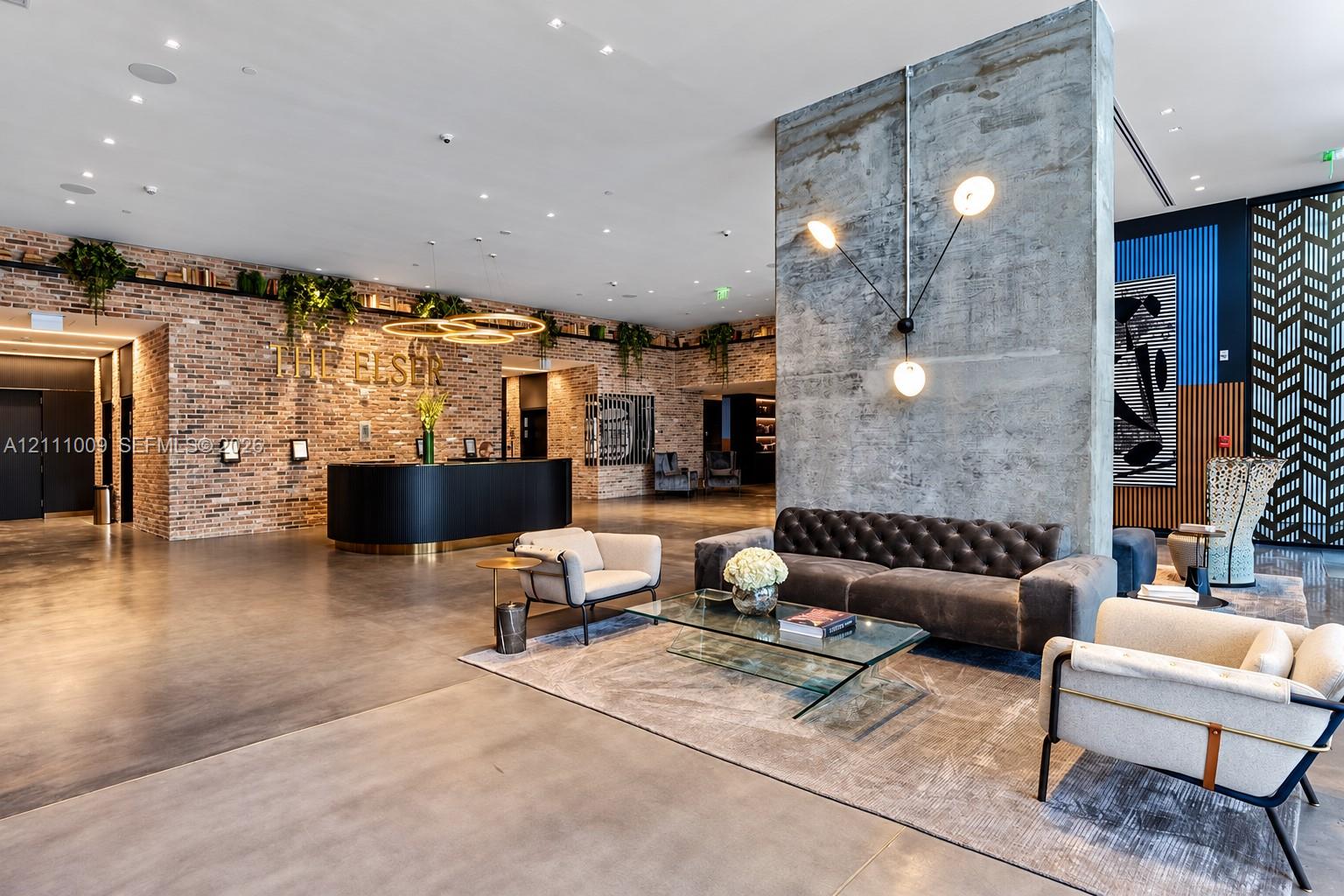 Expansive lobby featuring exposed brick walls, polished concrete flooring, a prominent concrete architectural pillar, and contemporary multi-arm wall lighting