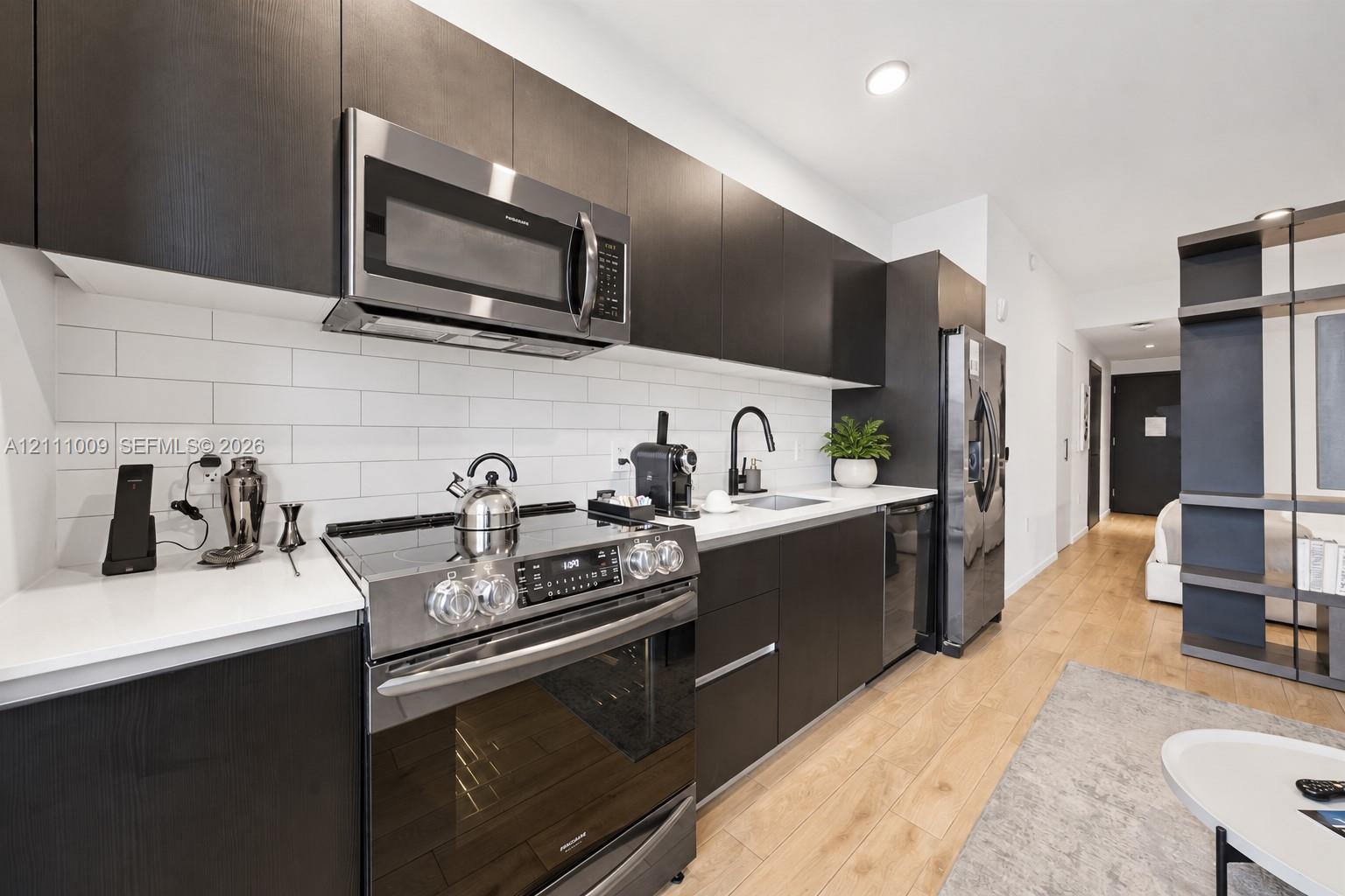 Kitchen featuring flat-panel dark cabinetry, white countertops, white subway tile backsplash, stainless steel appliances, and wood-finish flooring
