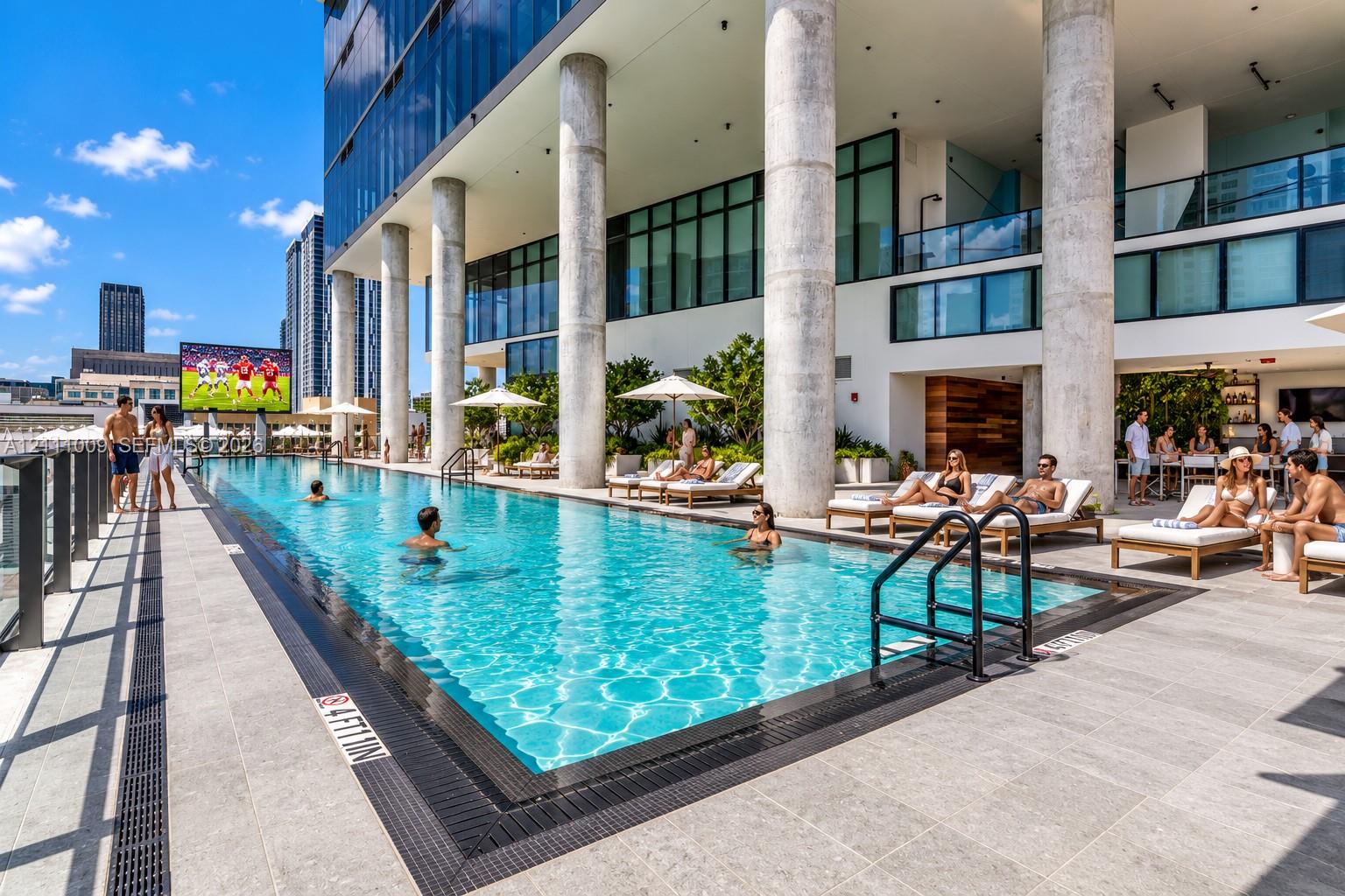 Expansive outdoor swimming pool featuring tile decking, structural concrete columns, glass exterior panels, and built-in drainage systems