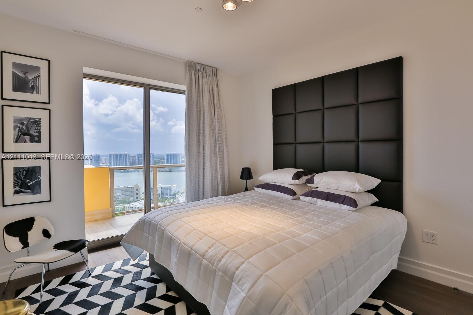 Floor-to-ceiling sliding glass door, private balcony with water scenery, and custom grid-tufted leather headboard
