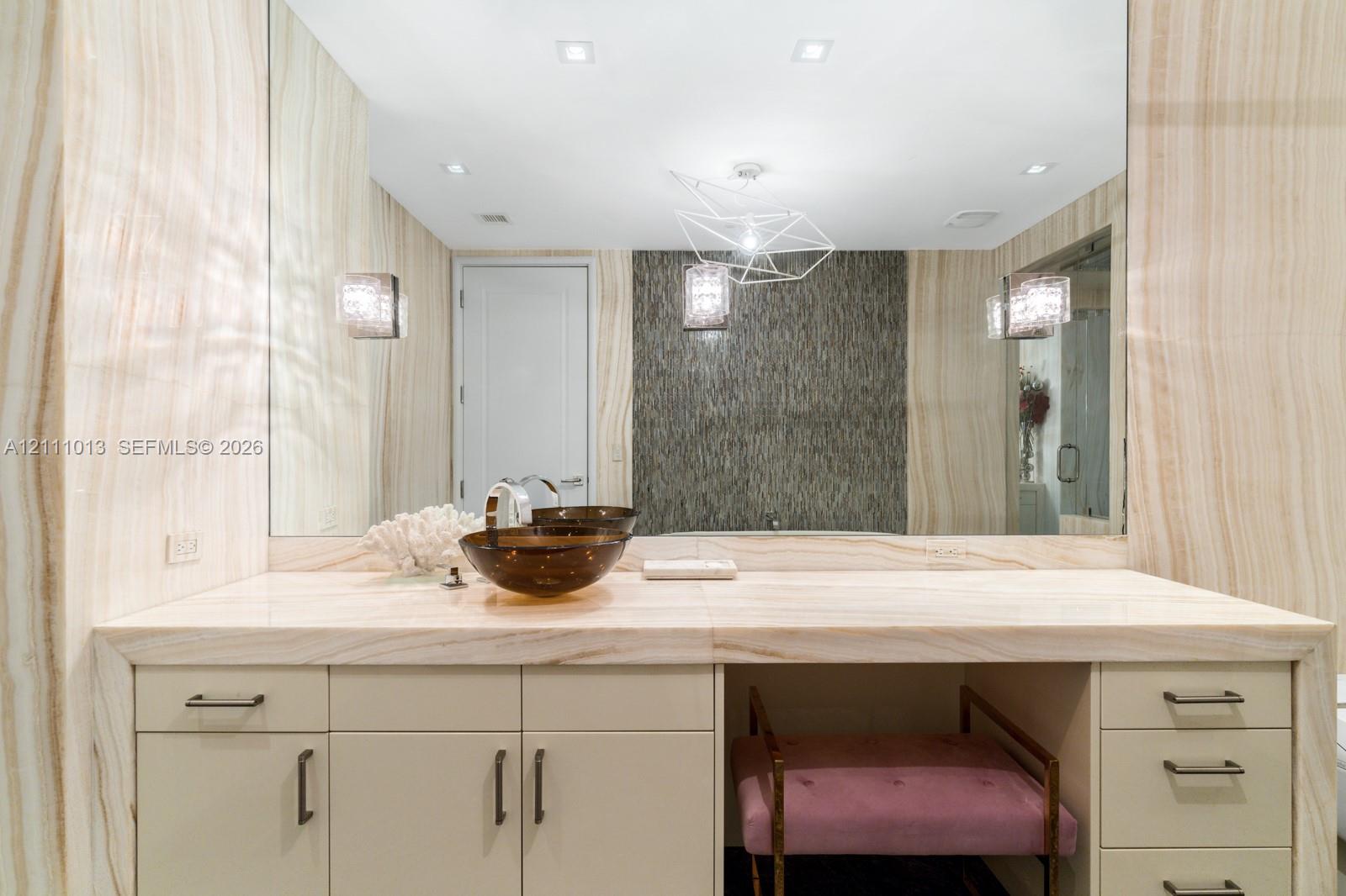 Custom vanity featuring a slab stone countertop, vessel sink, floor-to-ceiling stone wall cladding, geometric chandelier, and recessed lighting