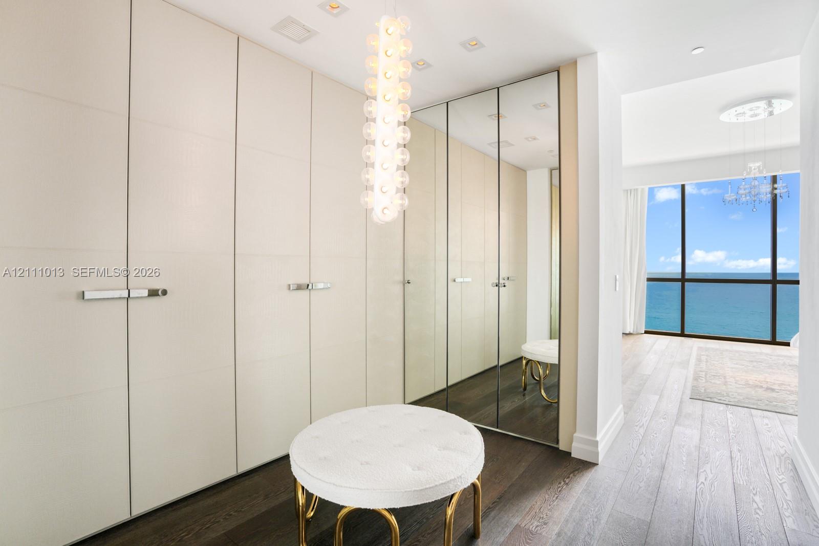Floor-to-ceiling built-in cabinetry with integrated hardware, mirrored closet doors, wood-finish flooring, custom pendant lighting, and floor-to-ceiling windows featuring an ocean horizon