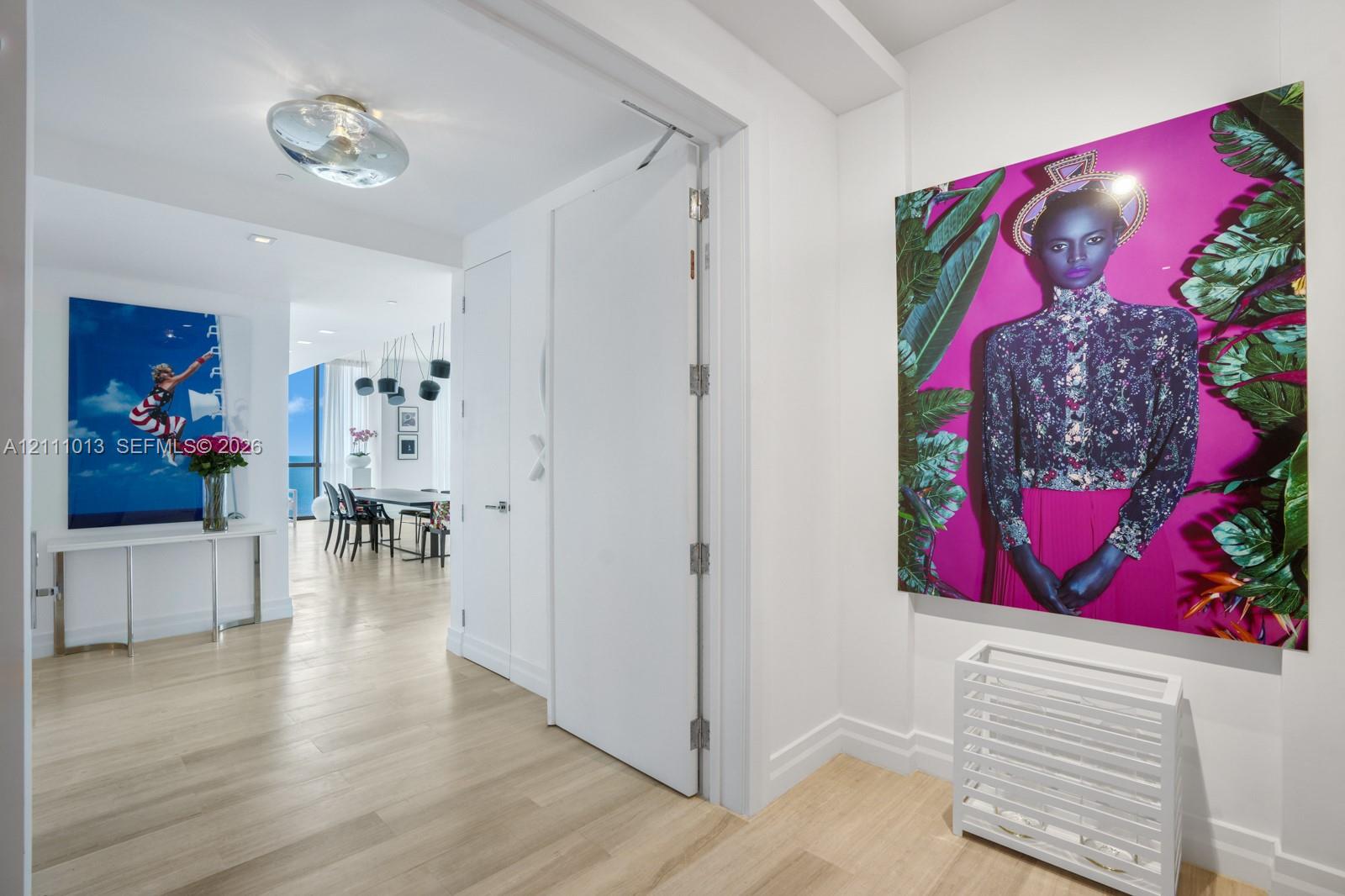Interior hallway featuring wood-finish flooring, smooth-finish walls, ceiling-mounted circular lighting, and a full-height interior door with metal hinges Interior hallway featuring wood-finish flooring, smooth-finish walls, ceiling-mounted circular lighting, and a full-height interior door with metal hinges
