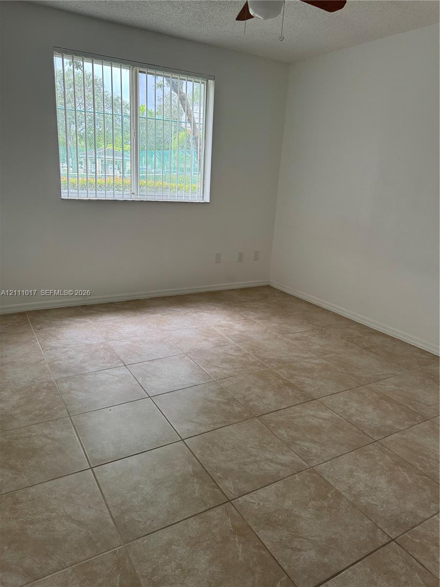 Neutral-toned ceramic tile flooring, multi-pane window with security bars, and a ceiling fan fixture