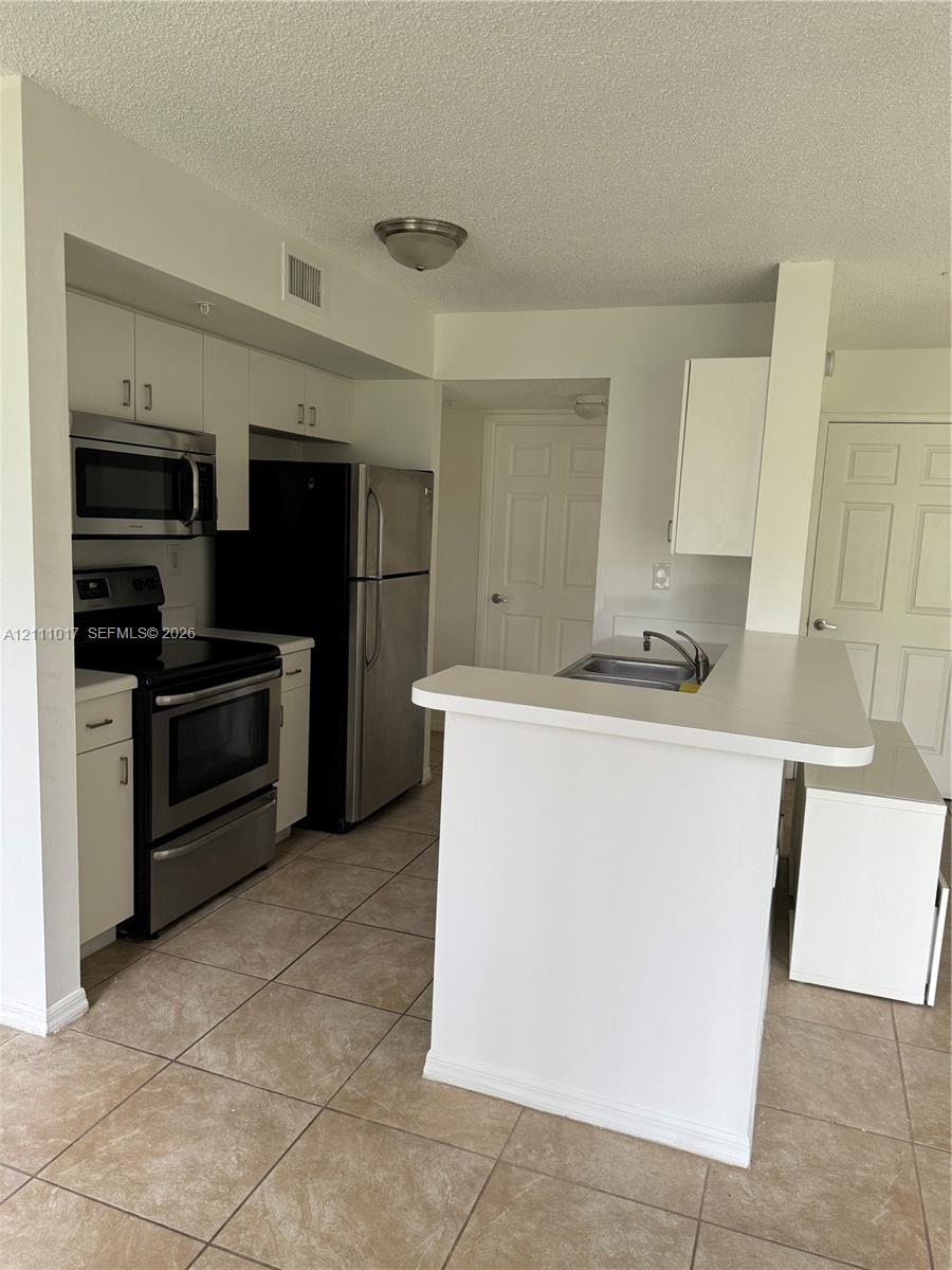 Kitchen featuring a breakfast bar, white cabinetry, tile flooring, and stainless steel appliances including a built-in microwave and range