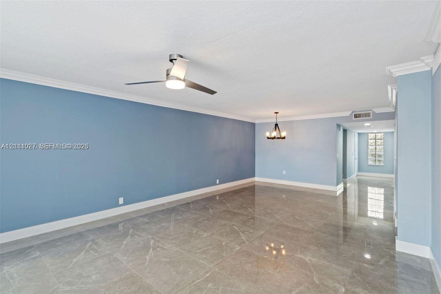 Large-format polished stone flooring, crown molding, modern three-blade ceiling fan with integrated light, and decorative multi-light chandelier Large-format polished stone flooring, crown molding, modern three-blade ceiling fan with integrated light, and decorative multi-light chandelier