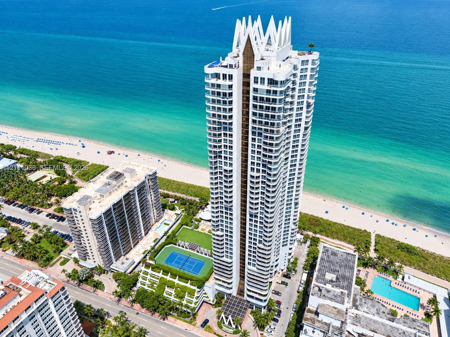 High-rise oceanfront tower featuring tiered architectural design, expansive balconies, a dedicated tennis court, and on-site swimming pools