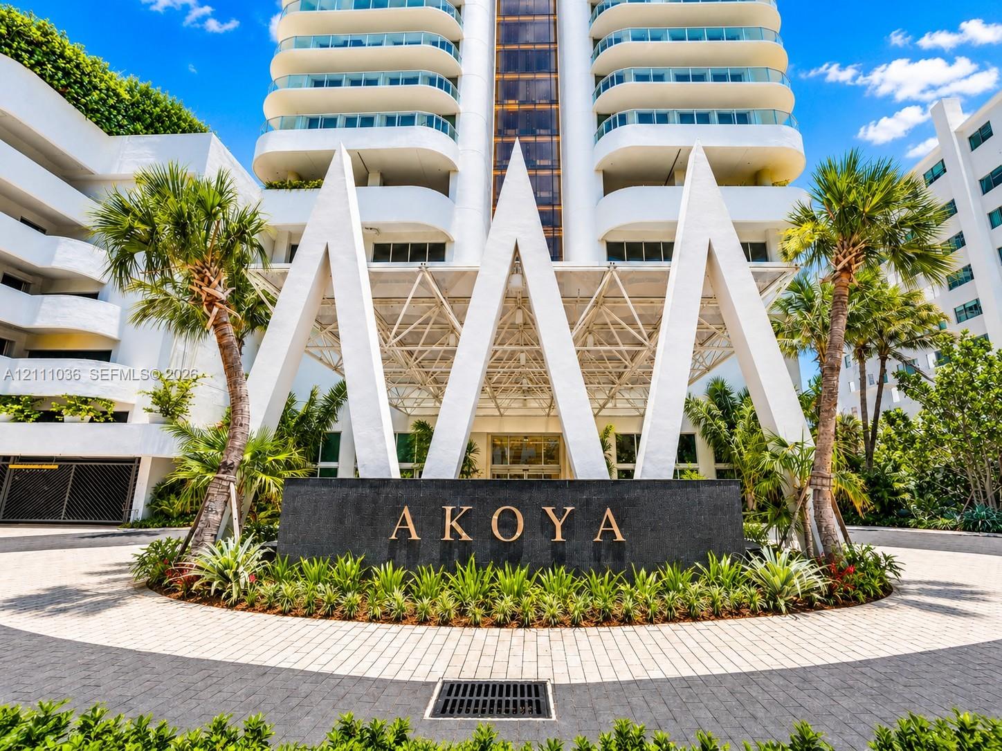 High-rise building featuring a geometric canopy entrance, stone-finished signage, curved balcony detailing, and a paver stone circular driveway