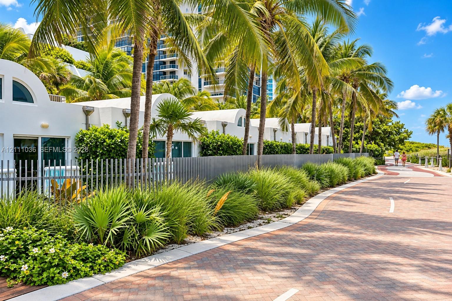 Stucco exterior featuring arched rooflines, integrated metal fencing, mature palm trees, and native ornamental landscaping situated along a paved brick path