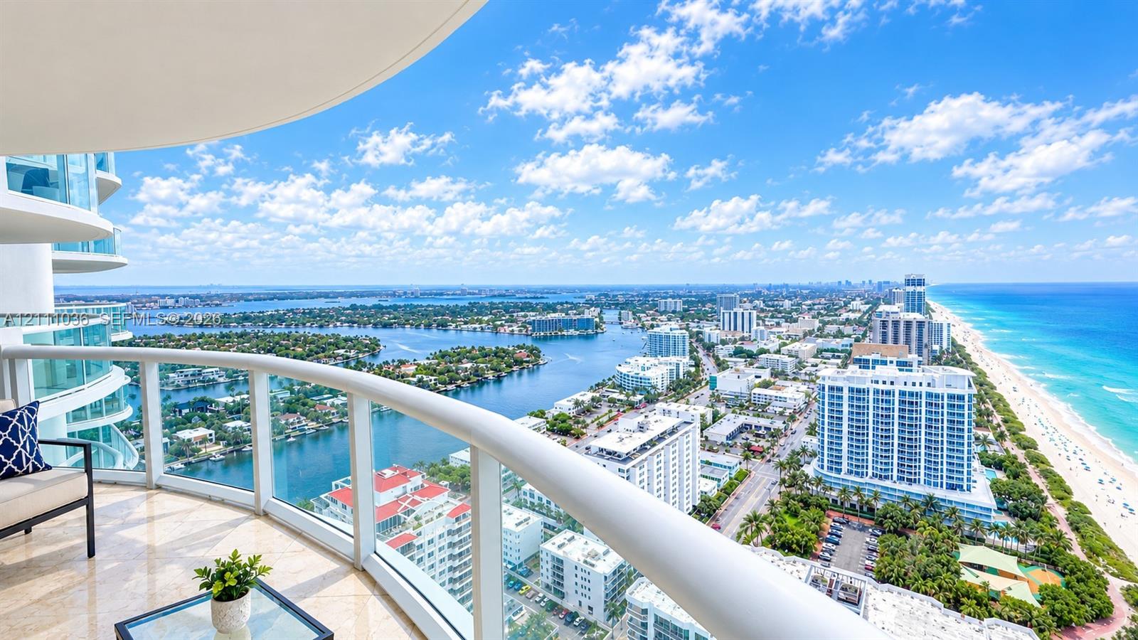 Curved covered balcony featuring stone flooring and glass-panel railings with expansive coastal and cityscape scenery