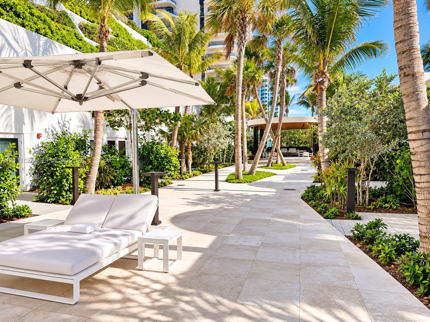 Outdoor patio featuring natural stone paving, mature palm trees, tiered tropical landscaping, and a covered pavilion
